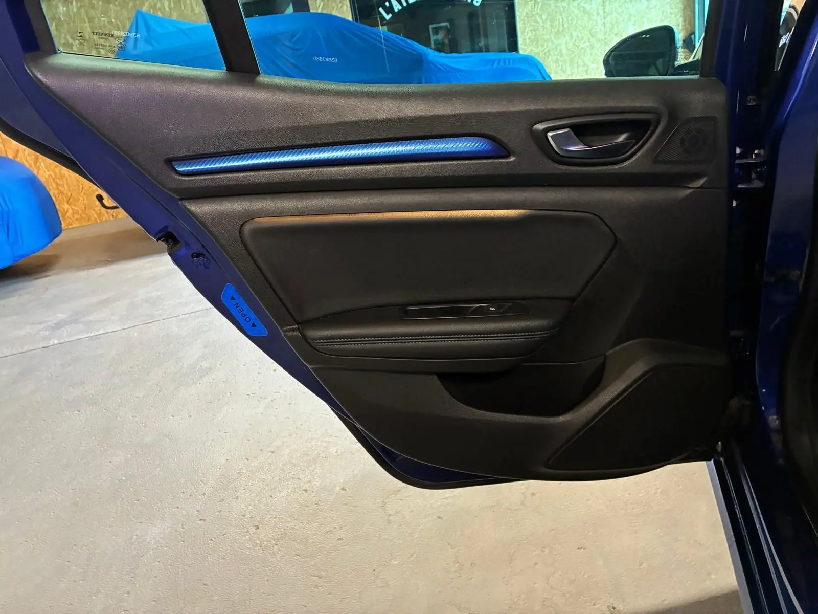 Vue rapprochée de la porte arrière gauche bleu foncé de la Renault Mégane 2019 avec insert décoratif bleu et poignée noire.