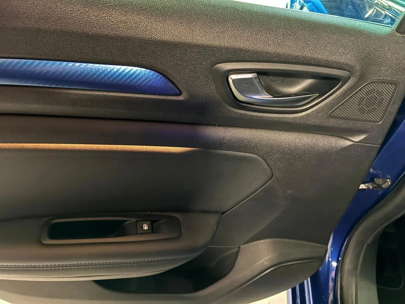 Vue rapprochée de la porte avant gauche d’une Renault Mégane bleu 2019, avec insert décoratif bleu et poignée intérieure chromée.