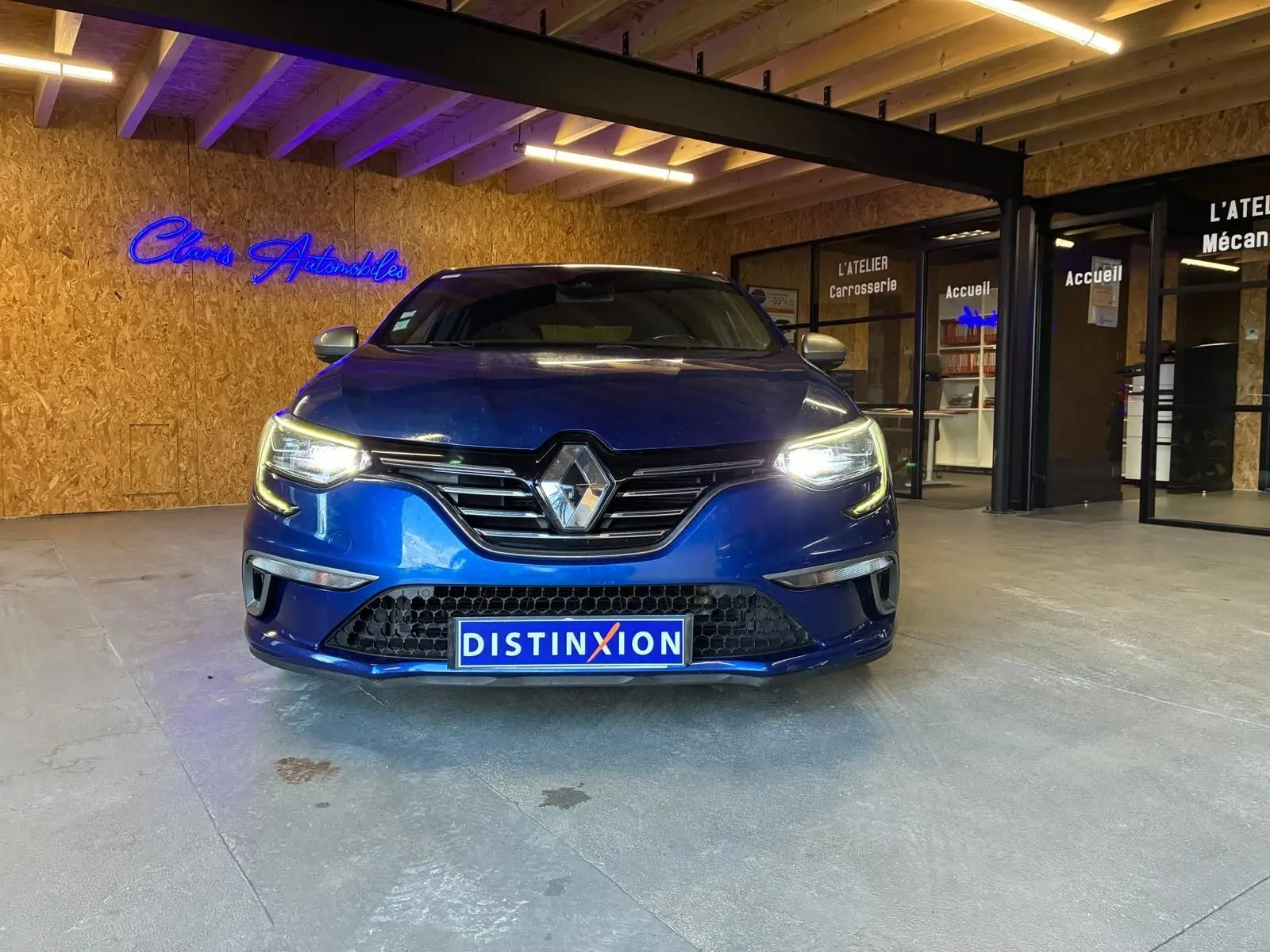 Vue frontale d'une Renault Mégane 1.7 BlueDCI 150 GT Line bleu avec phares allumés dans un showroom.