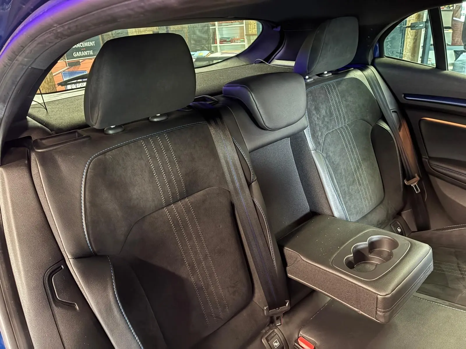 Vue intérieure arrière gauche des sièges noirs en cuir et alcantara de la Renault Mégane 2019 avec accoudoir central et porte-gobelets.