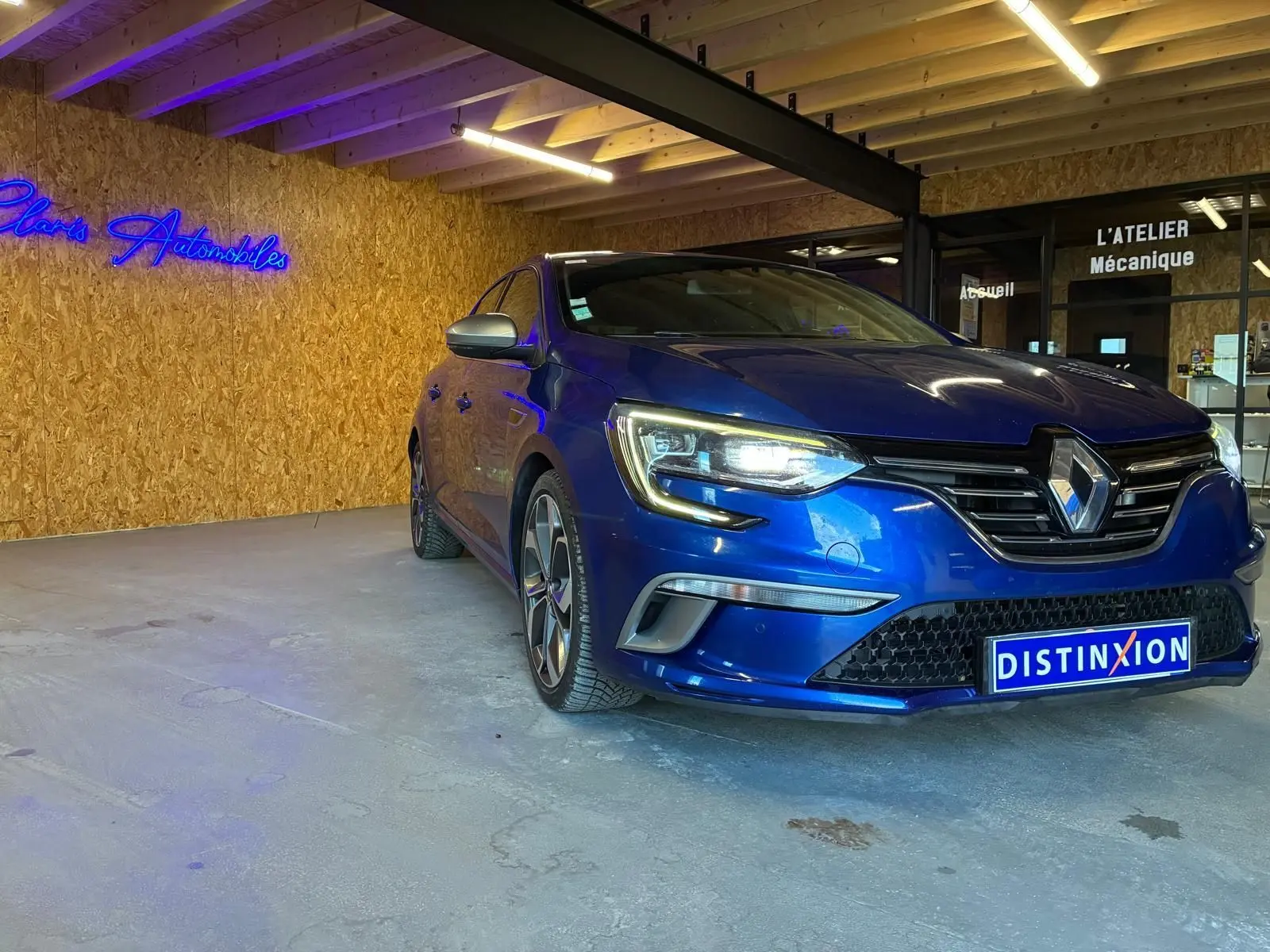 Renault Mégane 1.7 BlueDCI 150 GT Line bleu vue 3/4 avant droit, phare allumé en intérieur d'atelier.