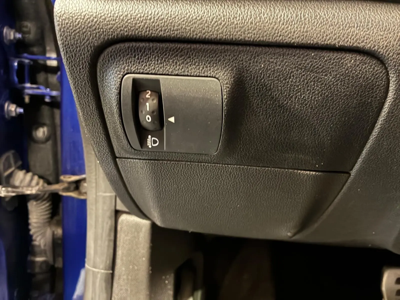 Gros plan sur le réglage d'inclinaison des phares côté gauche, avec une partie de la carrosserie bleu visible.