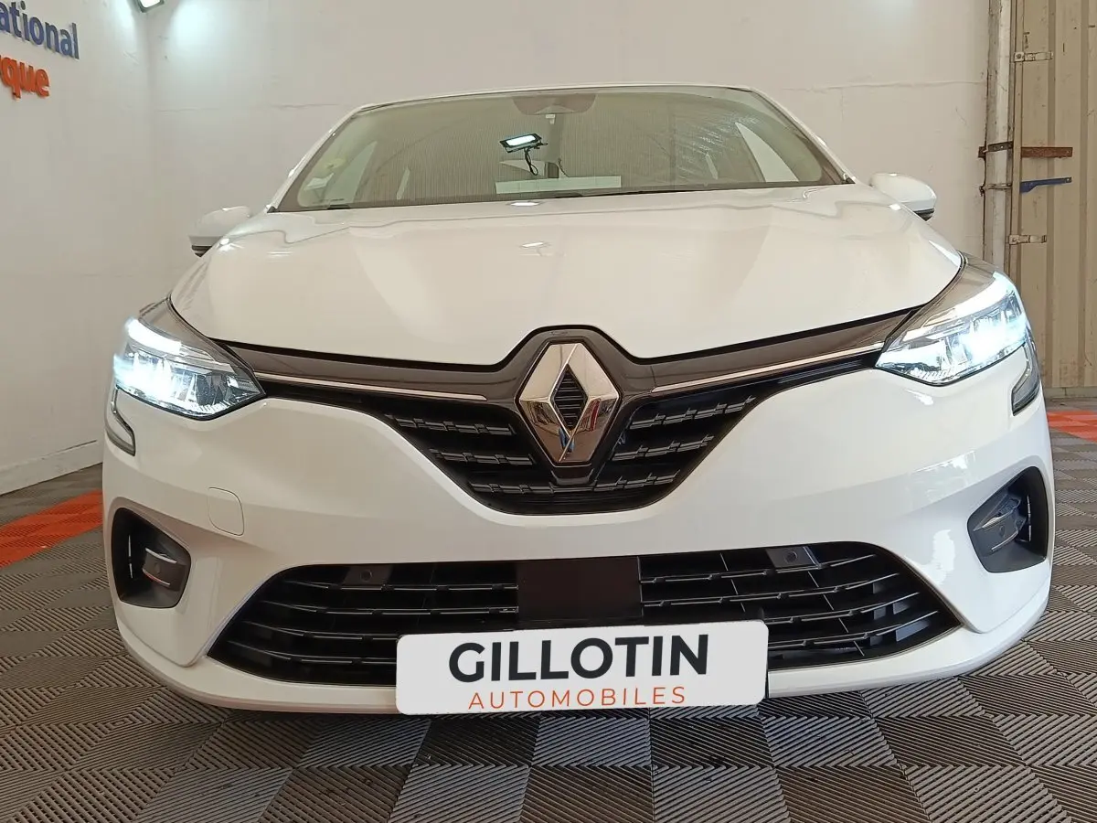 Vue avant d'une Renault Clio Business Blue dCi 100 blanche avec phares LED allumés dans un showroom.