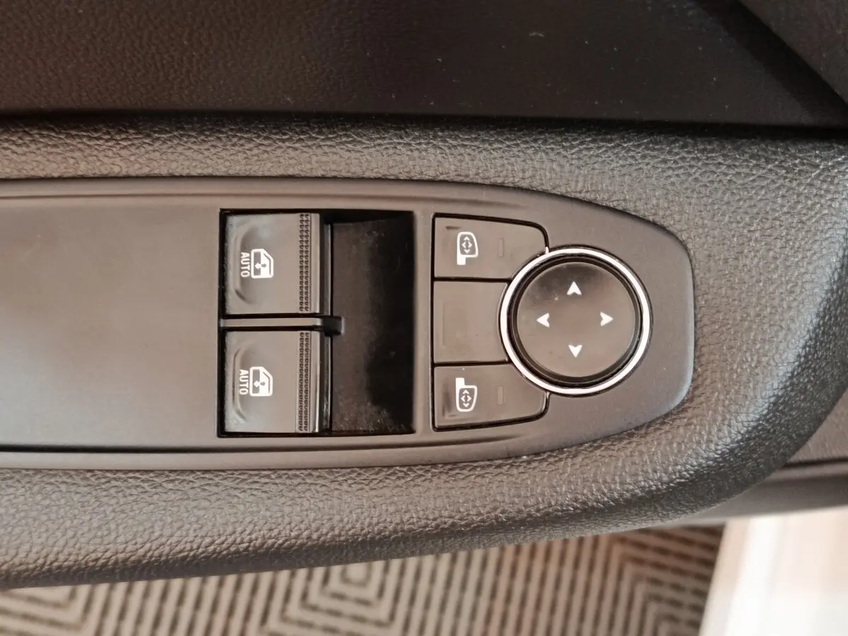 Gros plan sur les commandes de réglage des vitres et des rétroviseurs sur la porte côté conducteur d'une Renault Clio blanche.