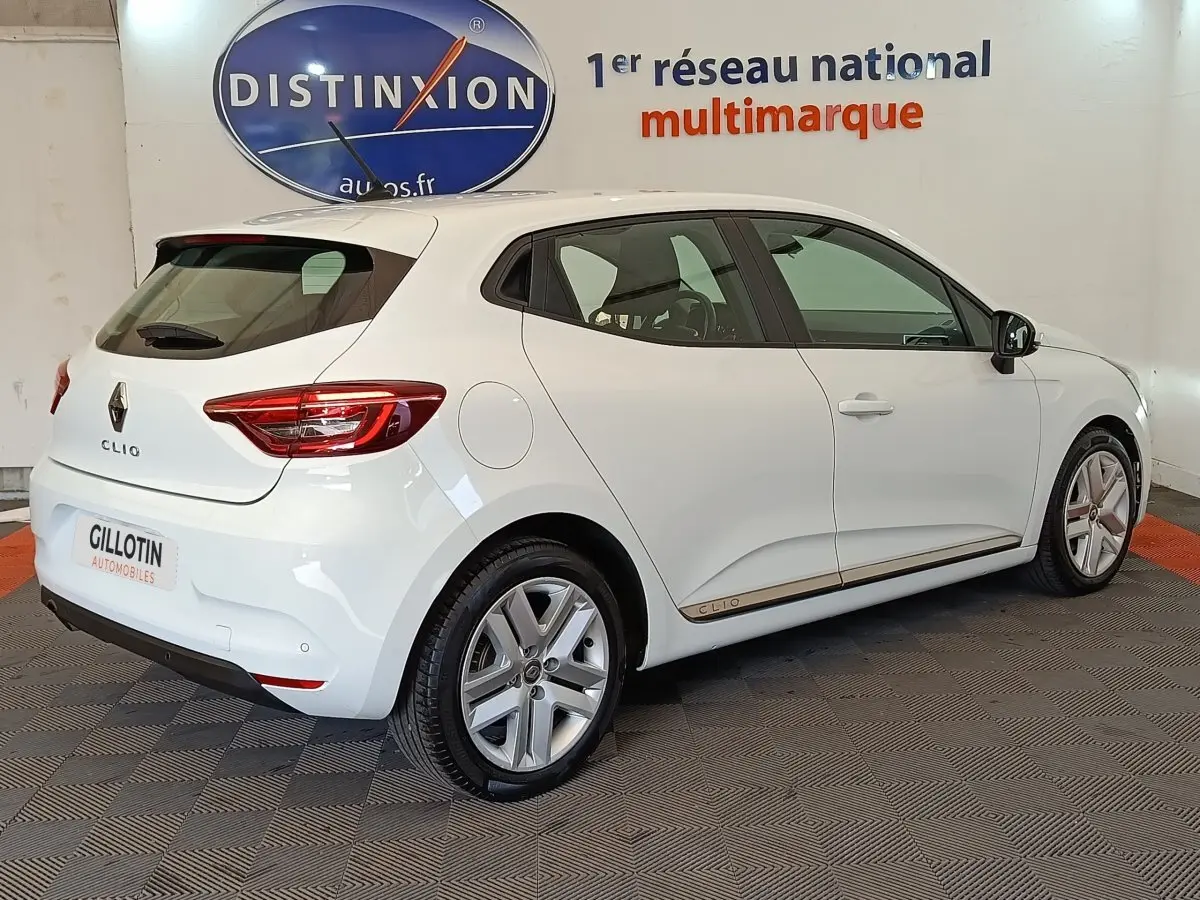 Vue 3/4 arrière droite d'une Renault Clio Business Blue dCi 100 blanche, avec jantes alliage et logo distinctif sur la porte.