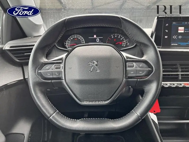 Vue rapprochée du volant cuir noir de la Peugeot 208 gris Artense avec commandes intégrées et tableau de bord numérique.