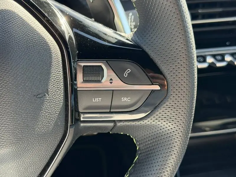 Gros plan sur les commandes gauche du volant cuir perforé du Peugeot 2008 gris, avec boutons LIST, SRC et téléphone.