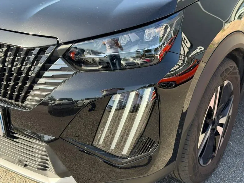 Gros plan sur le phare avant droit et la calandre d'une Peugeot 2008 gris Selenium avec jante alu noire.