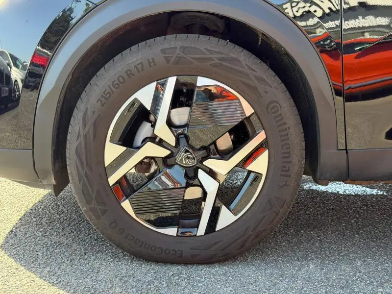 Gros plan sur la roue avant droite noire avec jante alu bicolore et logo Peugeot au centre sur un Peugeot 2008 gris.