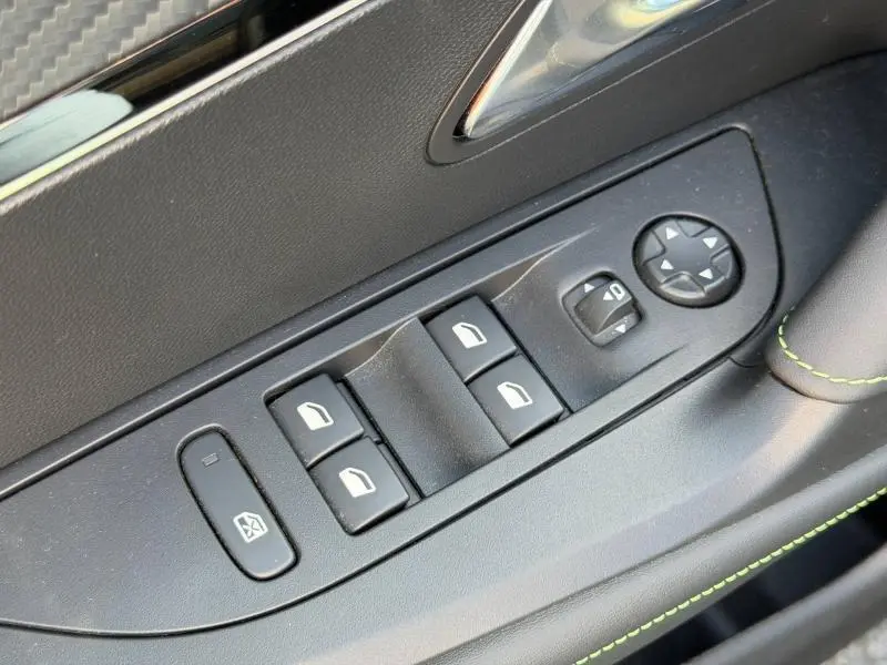 Détail des commandes de lève-vitres et rétroviseurs côté conducteur de la Peugeot 2008 gris, avec surpiqûres vertes.
