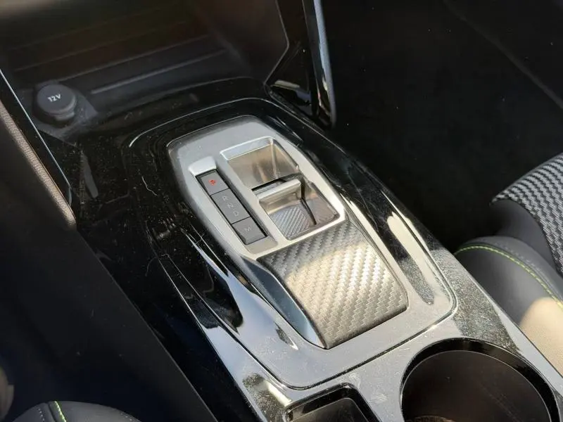 Gros plan sur la console centrale noire brillante avec levier de boîte auto et finition carbone dans un Peugeot 2008 gris.