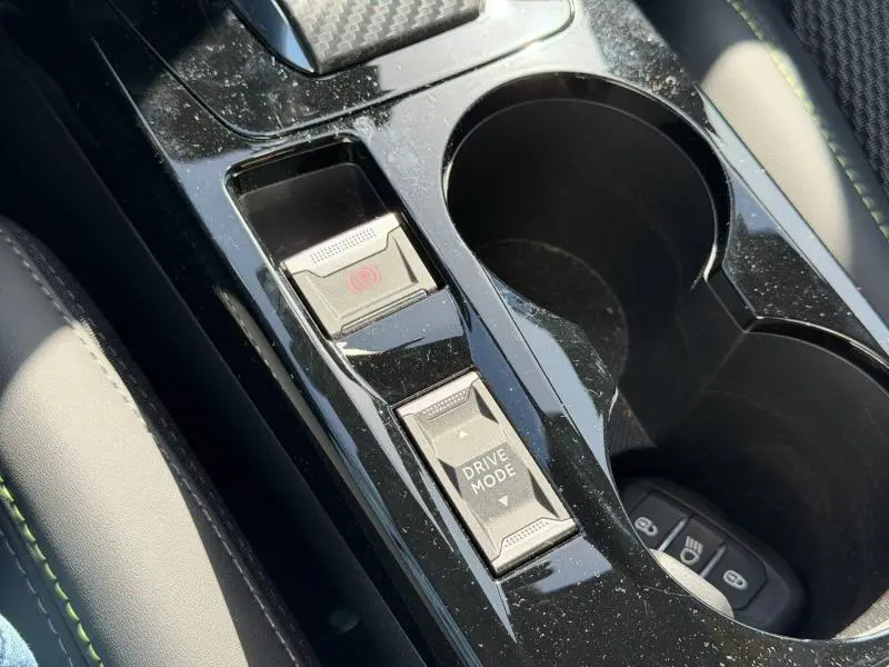 Gros plan sur la console centrale noire brillante du Peugeot 2008 gris, montrant le bouton Drive Mode et frein à main électrique.
