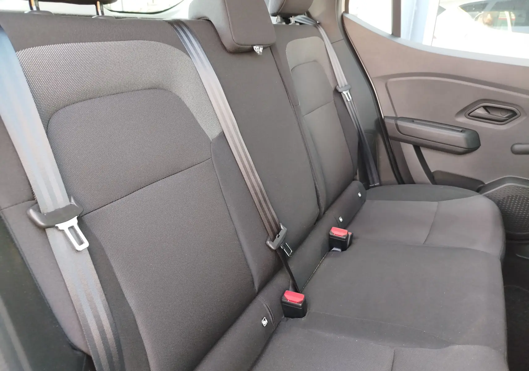 Vue latérale droite de la banquette arrière en tissu gris foncé de la Dacia Sandero 2025, avec ceintures et appuie-têtes visibles.