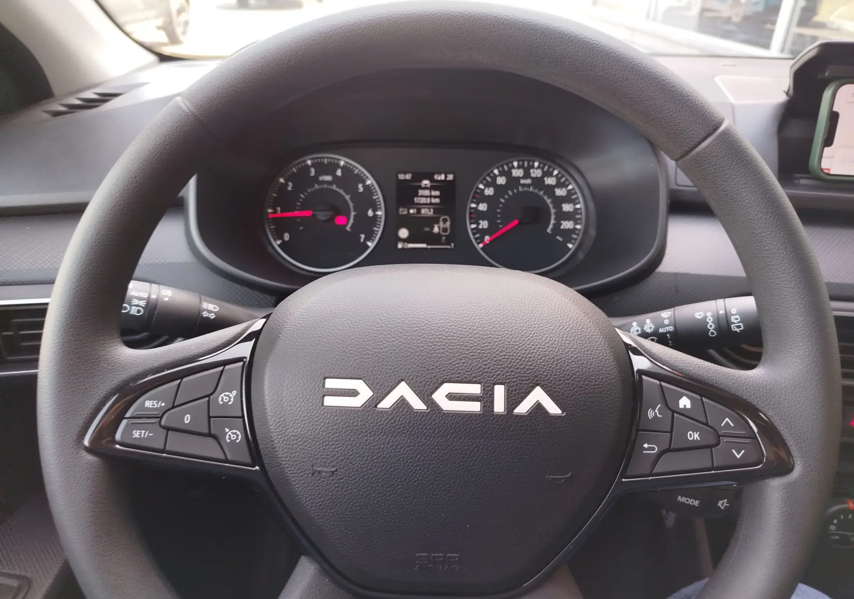 Vue rapprochée du volant noir de la Dacia Sandero 2025 avec commandes intégrées et tableau de bord en arrière-plan.