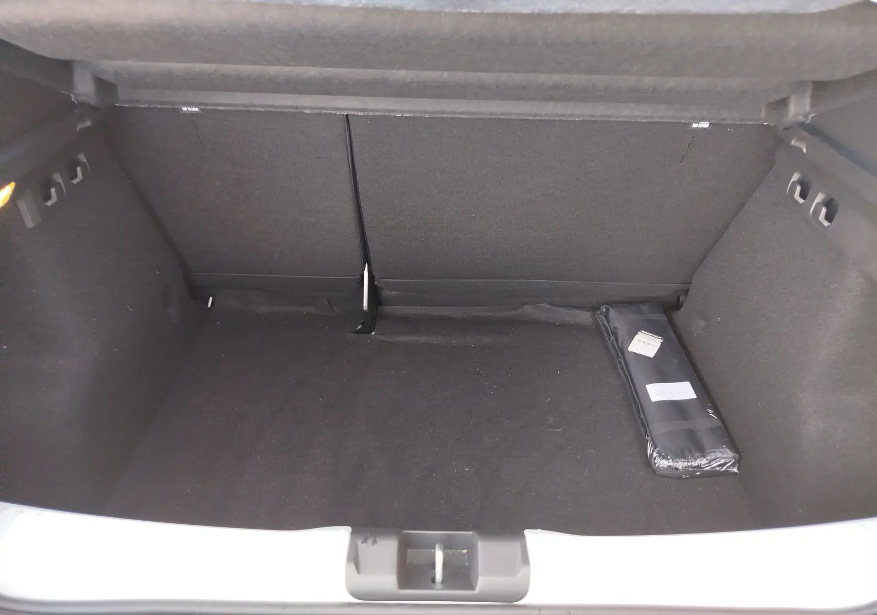 Coffre ouvert d'une Dacia Sandero Blanc Glacier, vue intérieure montrant un espace de rangement vide avec un accessoire noir posé à droite.