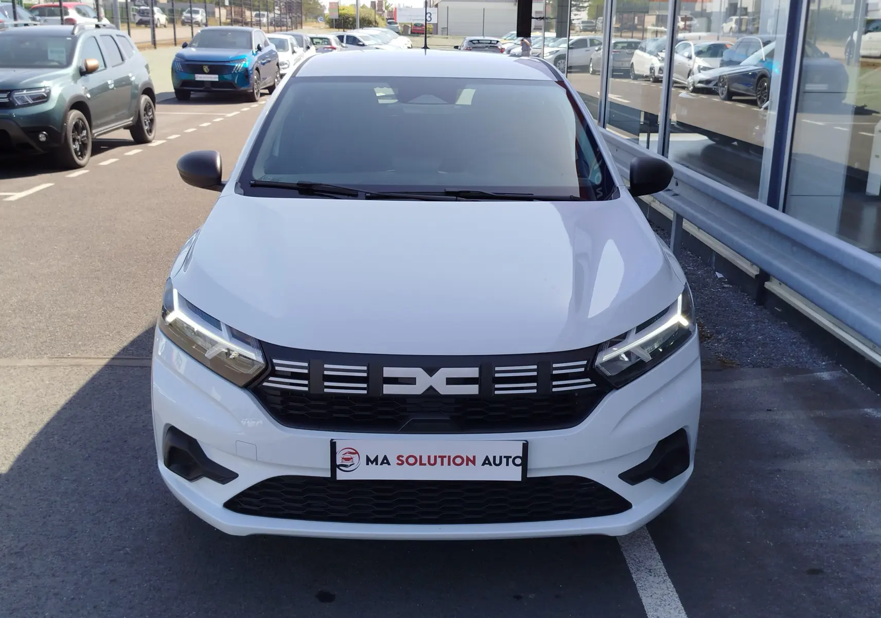 Vue avant frontale d'une Dacia Sandero blanche Glacier 2025 avec calandre noire et phares LED allumés.