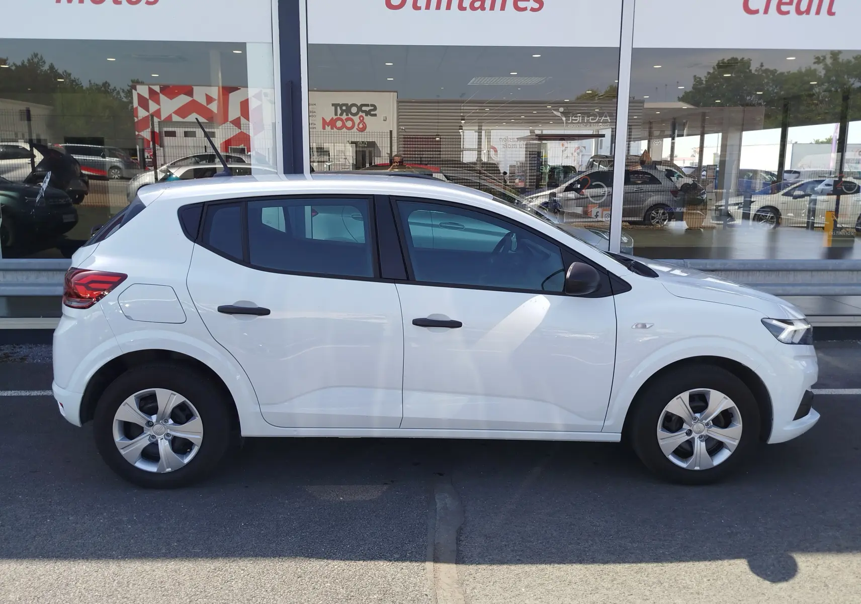 Vue de profil côté gauche d'une Dacia Sandero 2025 blanc glacier, compacte avec jantes alliage et poignées noires.