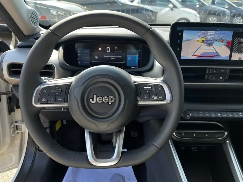 Vue intérieure centrée sur le volant Jeep d'un Avenger électrique blanc 2025 avec tableau de bord numérique et écran multimédia.