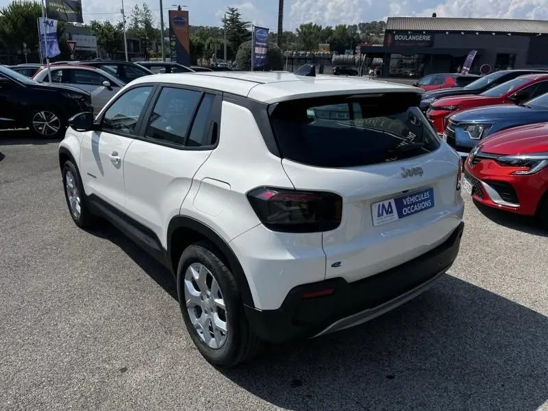 Jeep Avenger électrique blanc vu en 3/4 arrière droit, avec feux arrière foncés et toit noir contrastant.