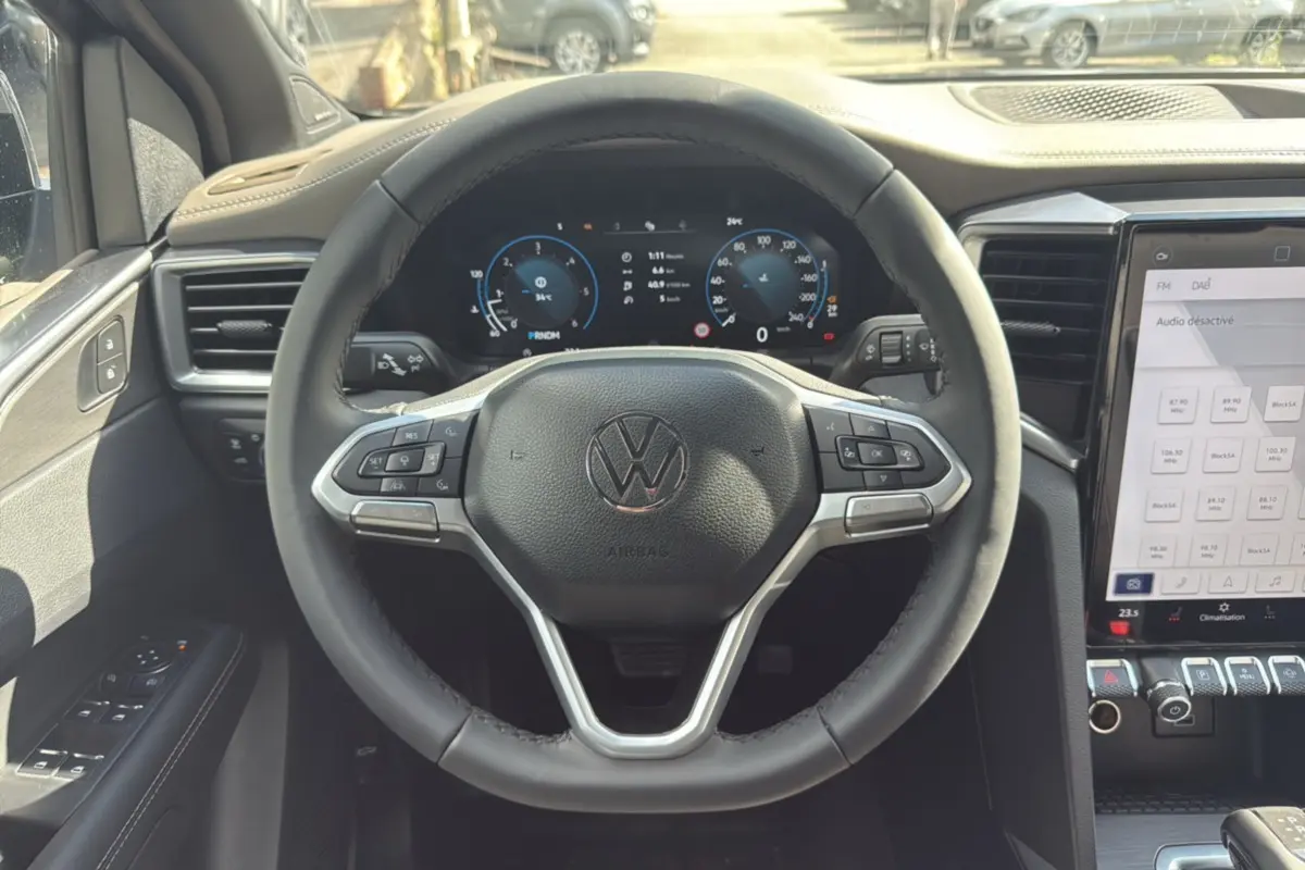 Vue intérieure centrée sur le volant noir du Volkswagen Amarok 2025 avec tableau de bord digital et écran tactile.