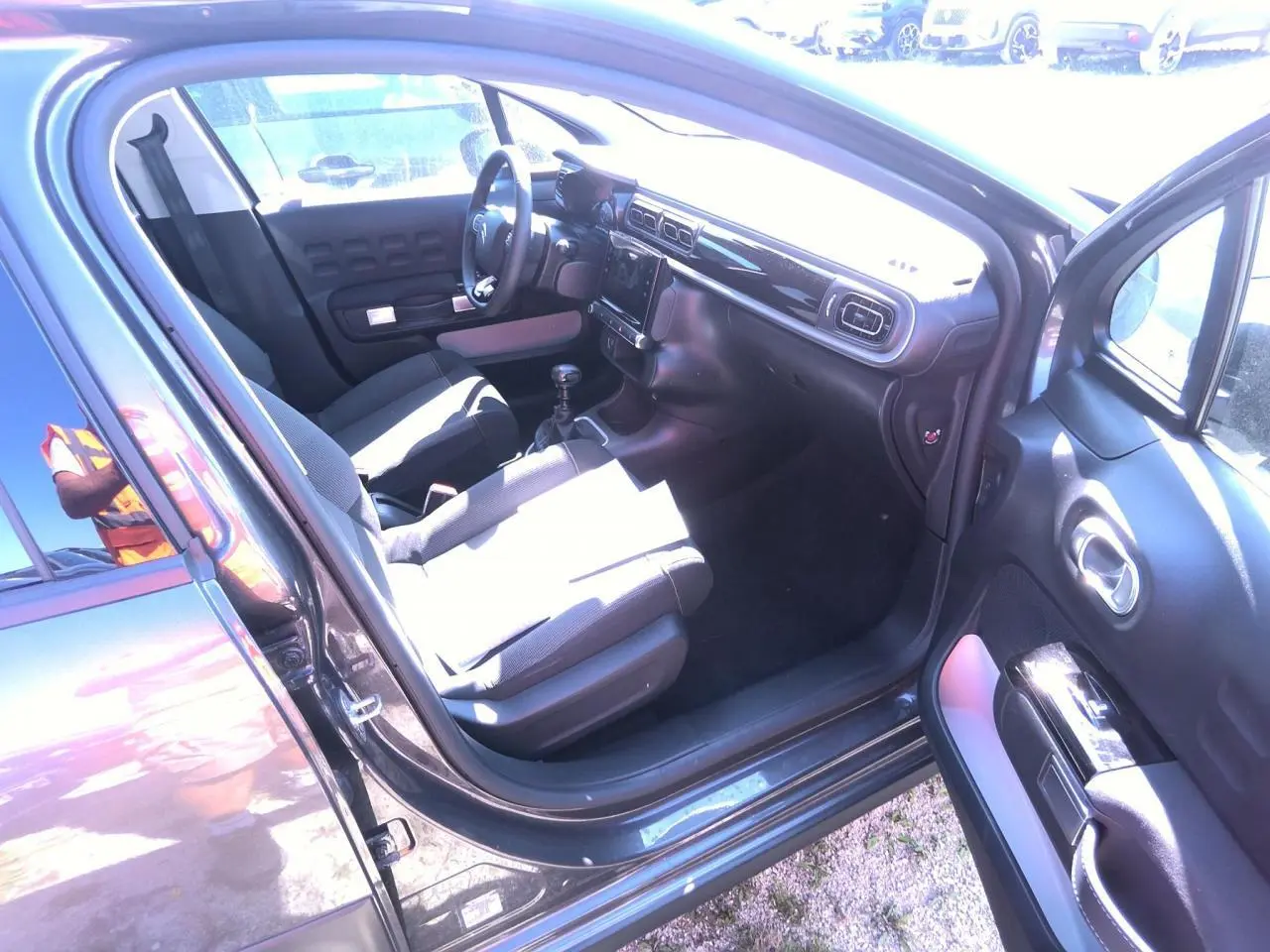 Intérieur côté conducteur de Citroën C3 gris foncé 2024, montrant sièges tissu gris et tableau de bord noir brillant.