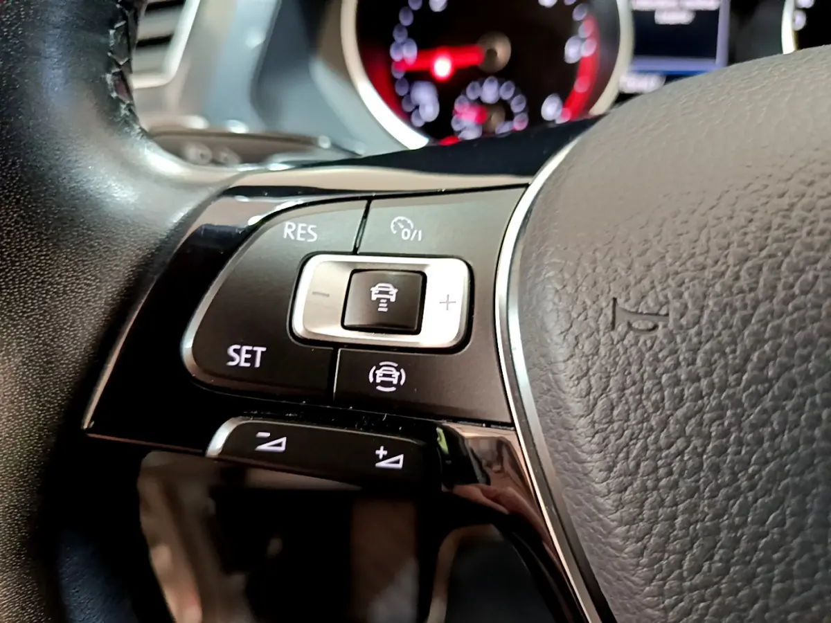 Gros plan sur les commandes du volant côté gauche du Volkswagen Tiguan gris clair, avec tableau de bord numérique en arrière-plan.