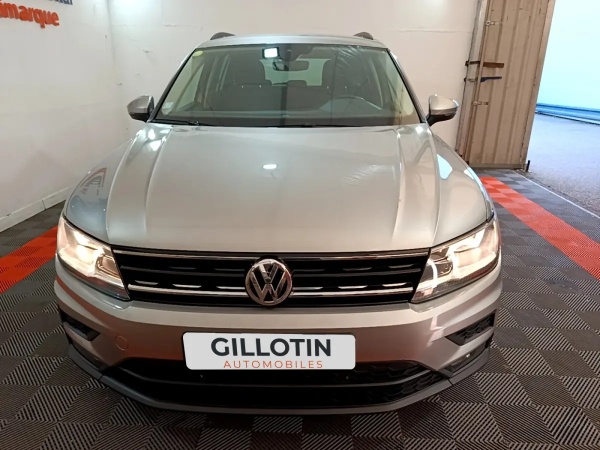 Vue frontale d'un Volkswagen Tiguan gris clair avec phares allumés et calandre noire brillante.