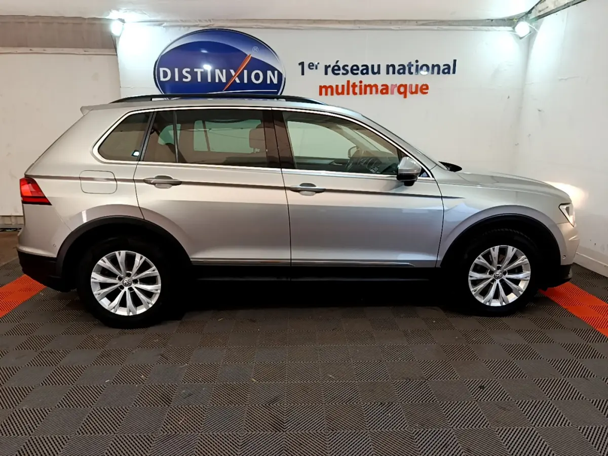 Profil côté gauche d'un Volkswagen Tiguan gris clair 2.0 TDI 150 DSG7 Confortline Business de 2020 en intérieur showroom.