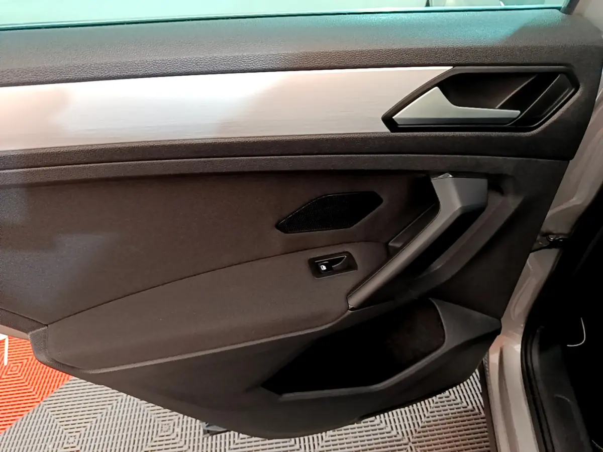 Vue rapprochée de la porte avant droite du Volkswagen Tiguan gris clair, avec poignée et commande de verrouillage intégrées.