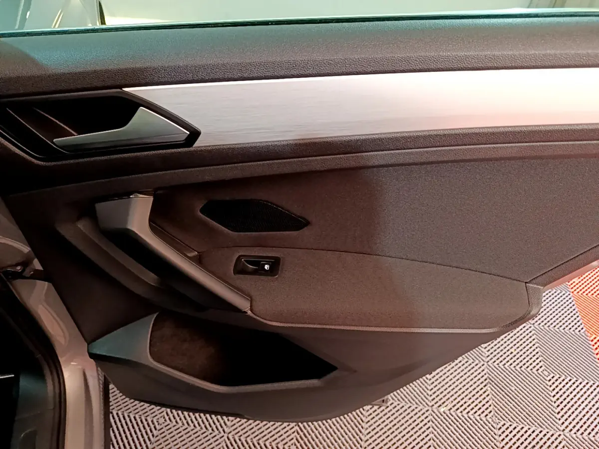 Vue intérieure du panneau de porte côté gauche du Volkswagen Tiguan gris clair, avec poignée argentée et haut-parleur intégré.