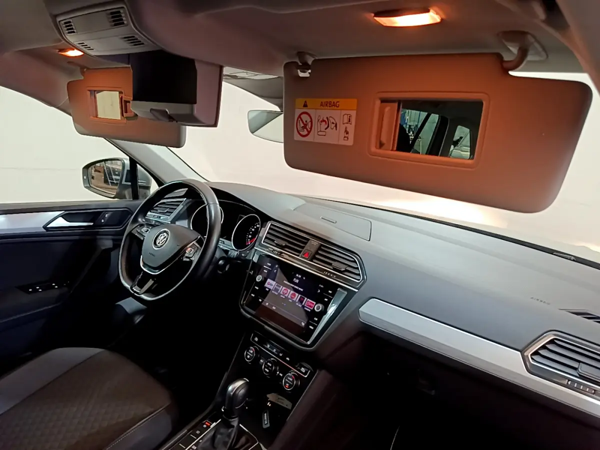 Intérieur du Volkswagen Tiguan 2020 vu côté conducteur, volant cuir, écran tactile et pare-soleil ouvert avec miroir.