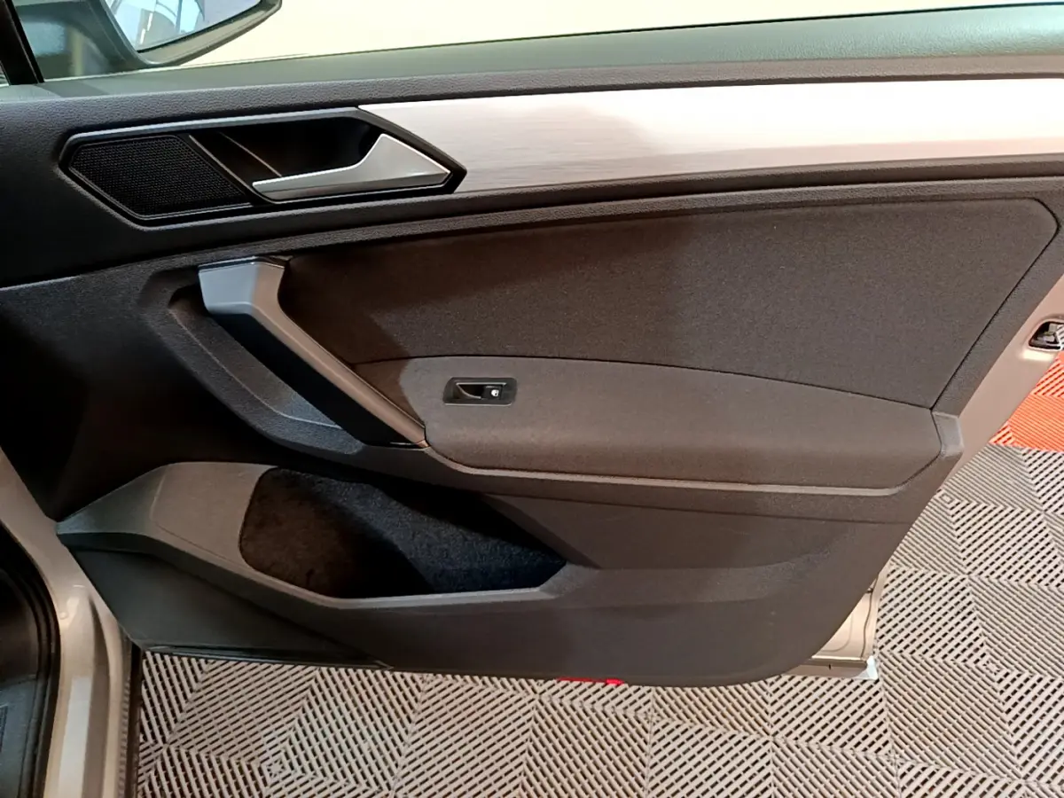 Vue rapprochée de la porte côté gauche du Volkswagen Tiguan gris clair, avec poignée et panneau noir mat.