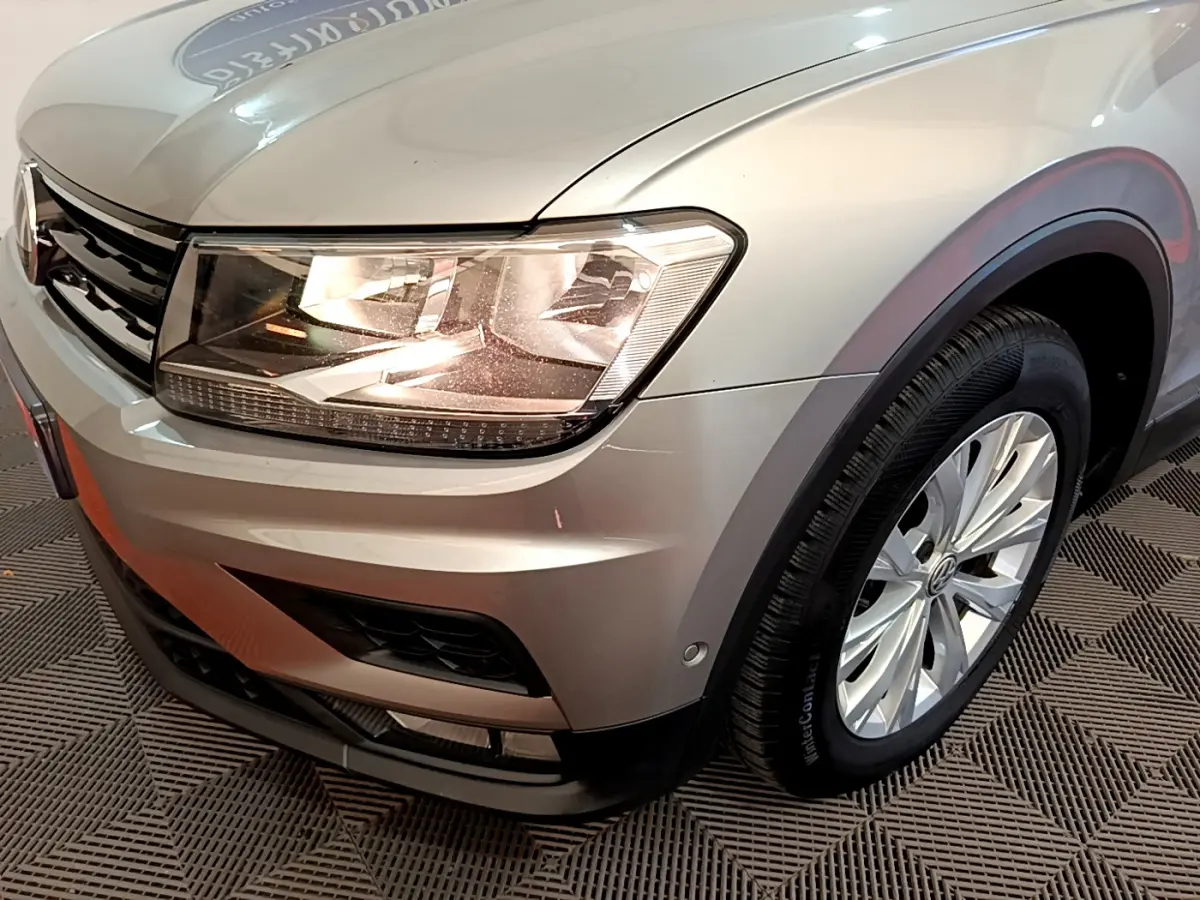 Gros plan sur l'avant droit gris clair du Volkswagen Tiguan 2.0 TDI 150 avec phare allumé et jante alu visible.
