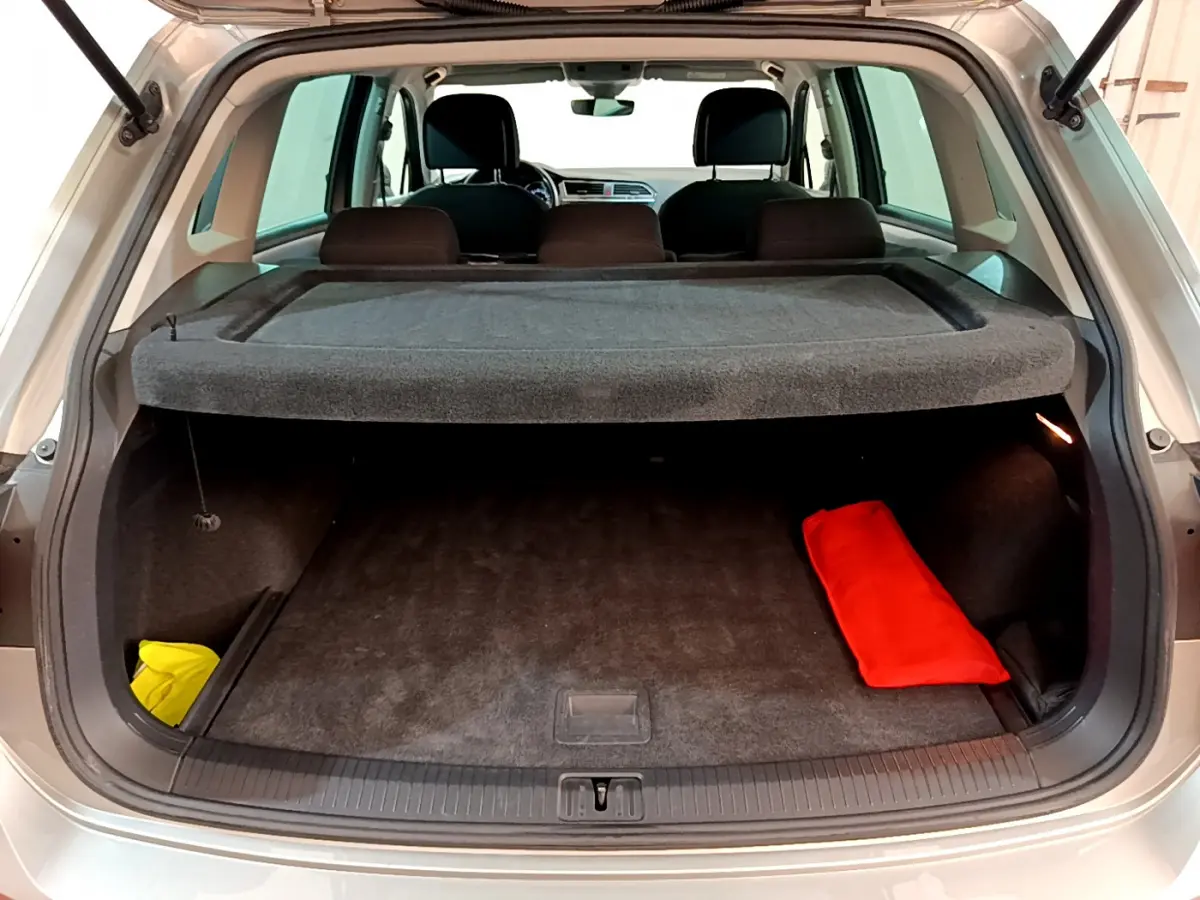 Coffre ouvert d'un Volkswagen Tiguan gris clair 2020, vue arrière avec cache-bagages et objets rouge et jaune visibles.