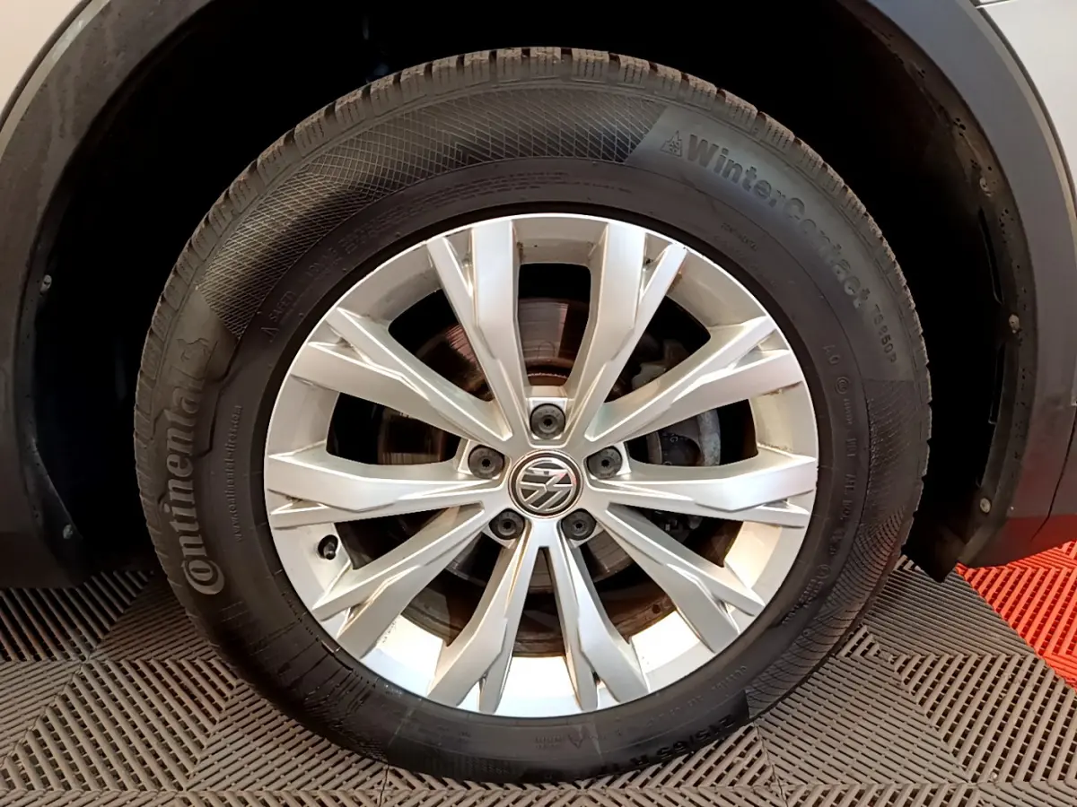 Gros plan sur la roue avant droite du Volkswagen Tiguan gris clair avec jante alliage et logo VW central.