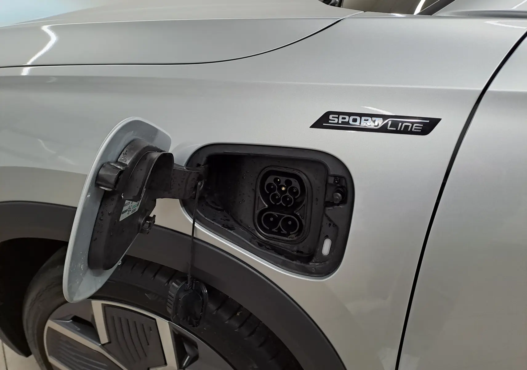 Prise de recharge ouverte côté gauche d’un Skoda Kodiaq Sportline gris argent avec jante alliage visible.
