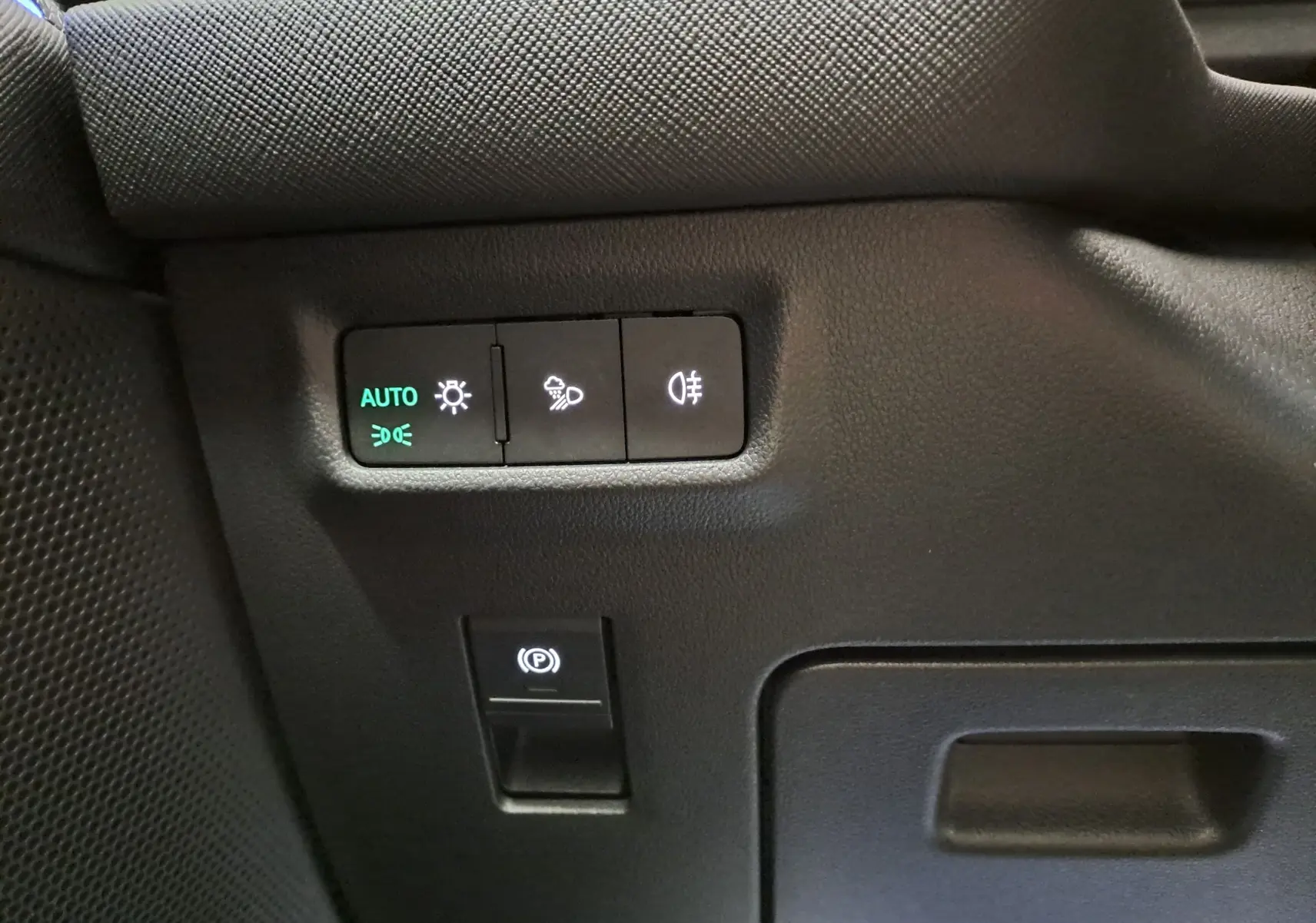 Détail intérieur du tableau de bord côté gauche du Skoda Kodiaq gris argent, boutons de réglage des phares et frein à main électrique.