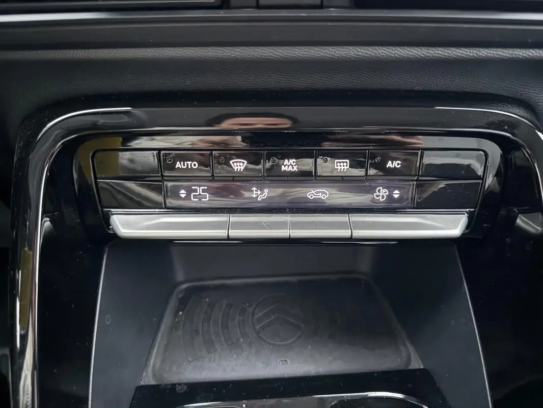 Gros plan sur la commande de climatisation automatique et le plateau de recharge sans fil noir dans une Citroën C3 gris 2025.