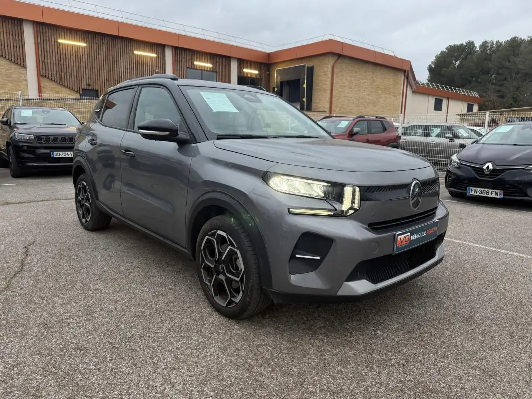 Vue 3/4 avant d'une Citroën C3 gris métallisé avec jantes alliage 17 pouces et barres de toit visibles.