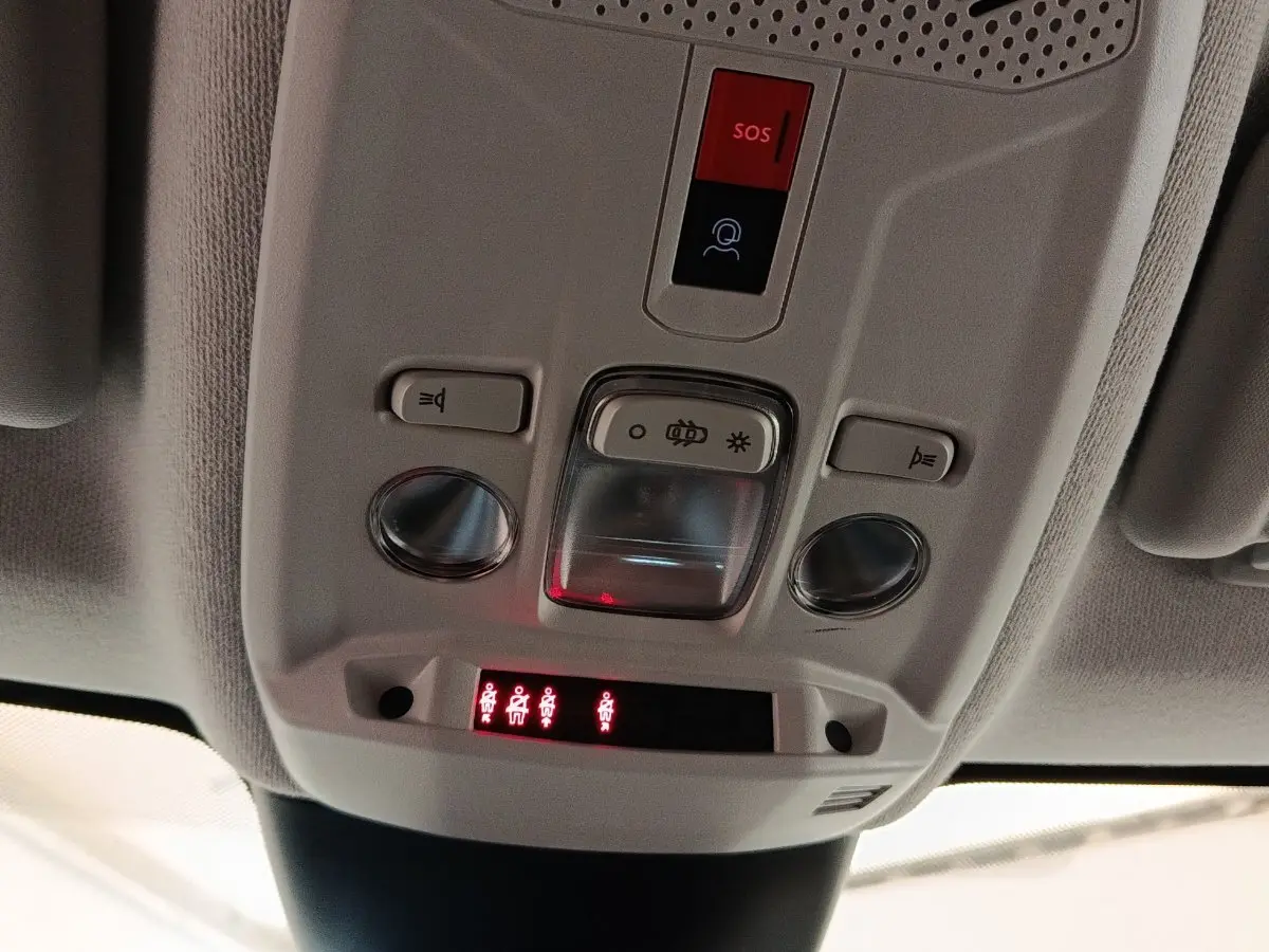 Gros plan sur la console de plafonnier gris clair avec boutons d’éclairage et indicateurs de ceinture allumés dans une Citroën C4 gris foncé.