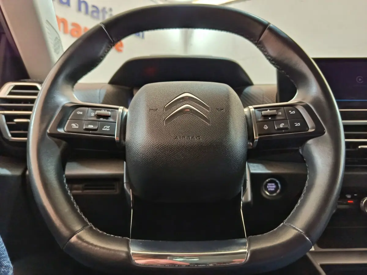 Gros plan sur le volant cuir noir du Citroën C4 2022 avec commandes multifonctions et bouton démarrage visible à droite.