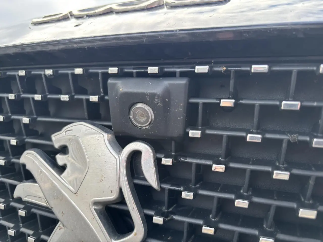 Gros plan sur la calandre noire du Peugeot 3008 2022, avec logo lion argenté et caméra frontale intégrée.