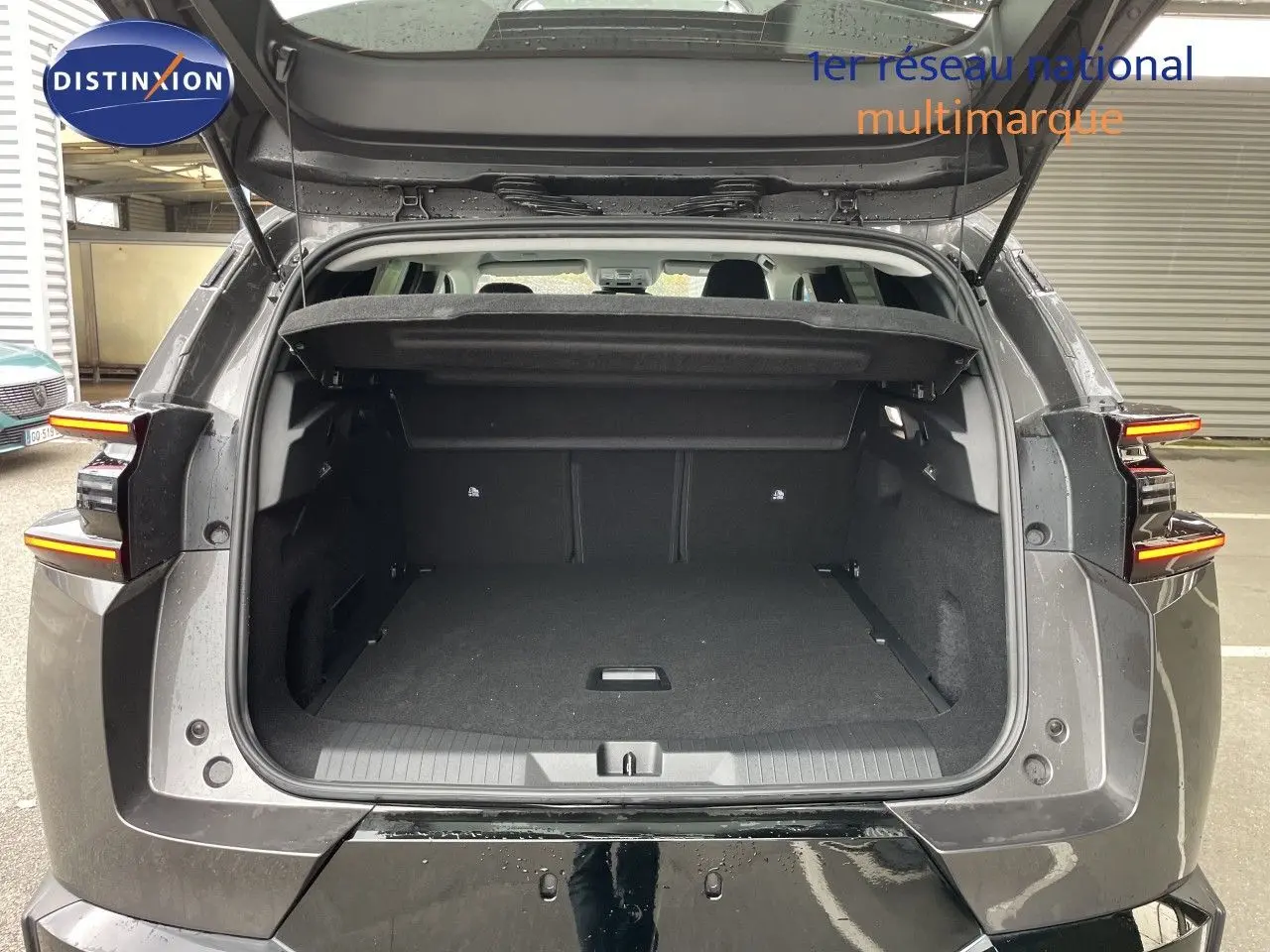 Coffre ouvert vu de l’arrière d’un Citroën C5 Aircross Hybrid gris platinium métal, feux arrière allumés.