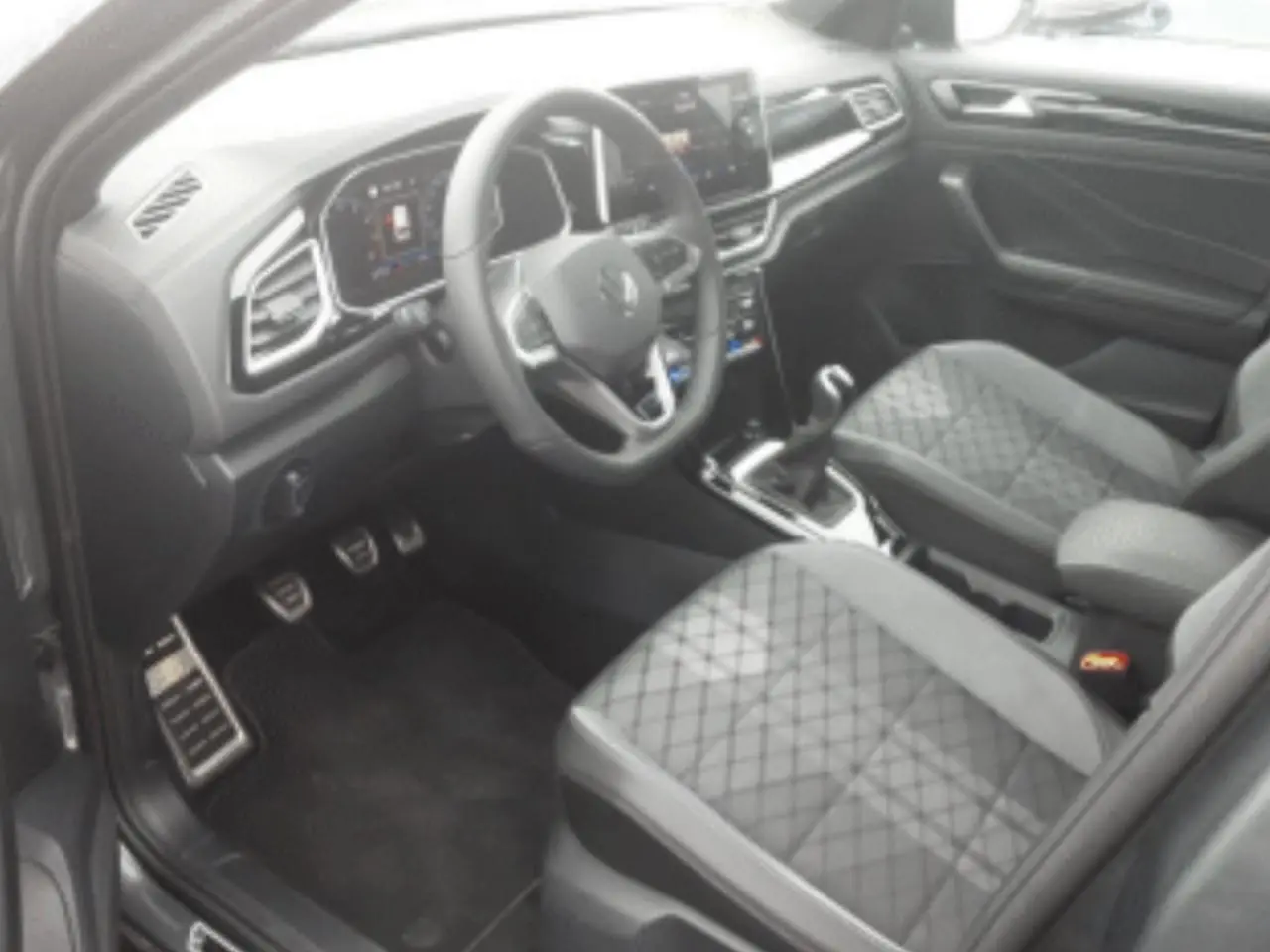 Vue intérieure côté conducteur du Volkswagen T-Roc gris platinium, mettant en valeur le volant multifonction et les sièges en tissu matelassé.