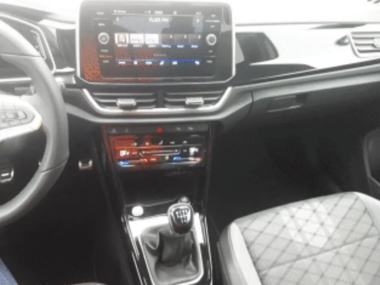 Vue intérieure centrée sur la console centrale du Volkswagen T-Roc gris platinium avec levier de vitesse manuel et écran tactile.