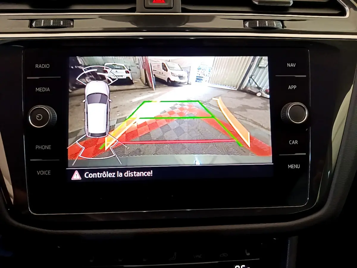 Écran tactile du tableau de bord montrant la caméra de recul avec alertes de distance du Volkswagen Tiguan gris clair.