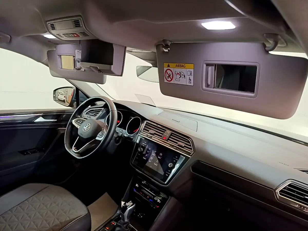 Intérieur du Volkswagen Tiguan gris clair vu côté conducteur, tableau de bord moderne avec écran tactile et volant cuir.