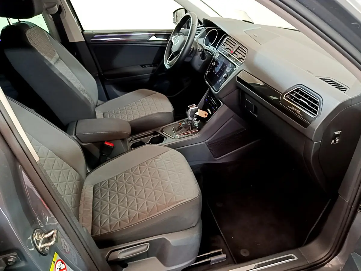 Intérieur avant du Volkswagen Tiguan gris clair, vue côté conducteur montrant sièges tissu et tableau de bord moderne.