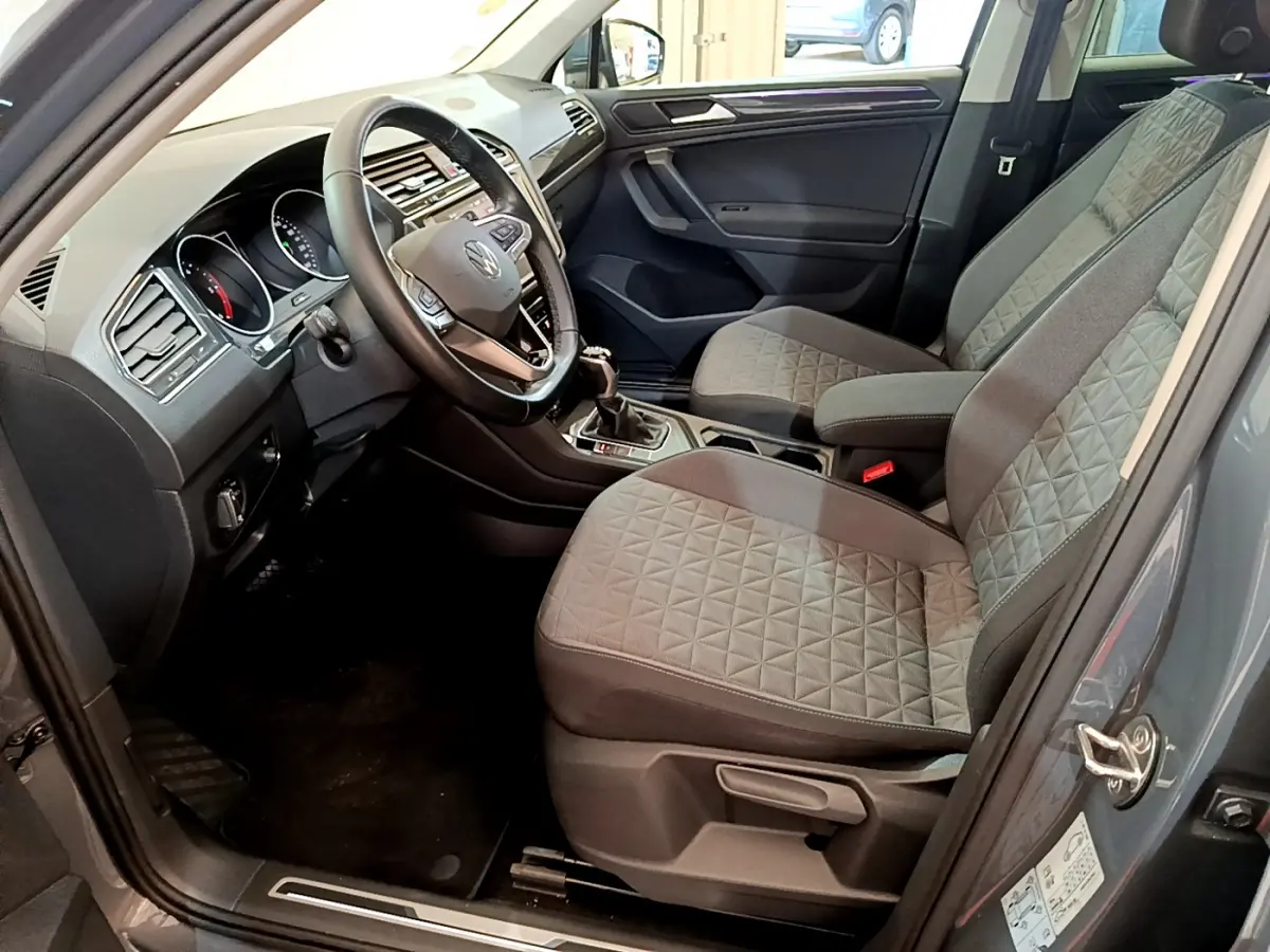 Vue intérieure côté conducteur du Volkswagen Tiguan gris clair 2021, sièges tissu à motifs géométriques et volant cuir multifonctions.