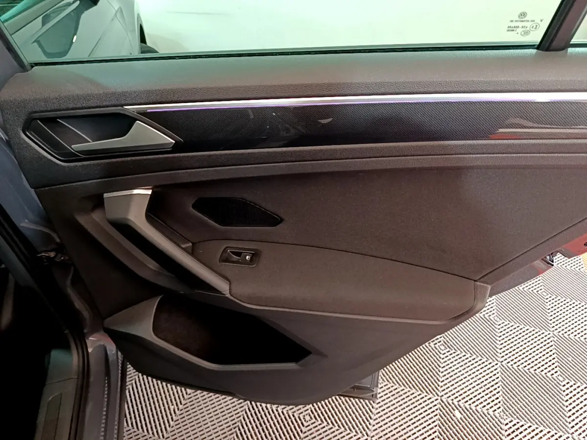 Vue intérieure côté gauche de la porte avant gris clair du Volkswagen Tiguan avec poignée argentée et garniture noire.
